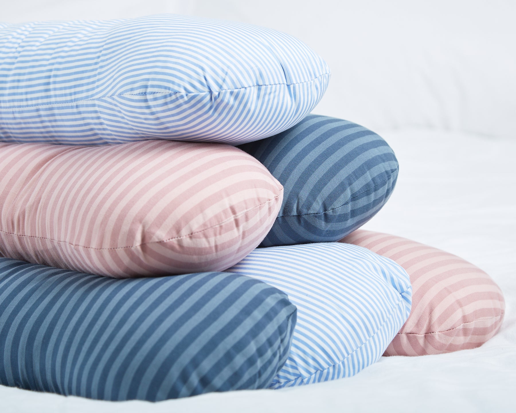 Weighted sleep pillows in different colours stacked on a bed